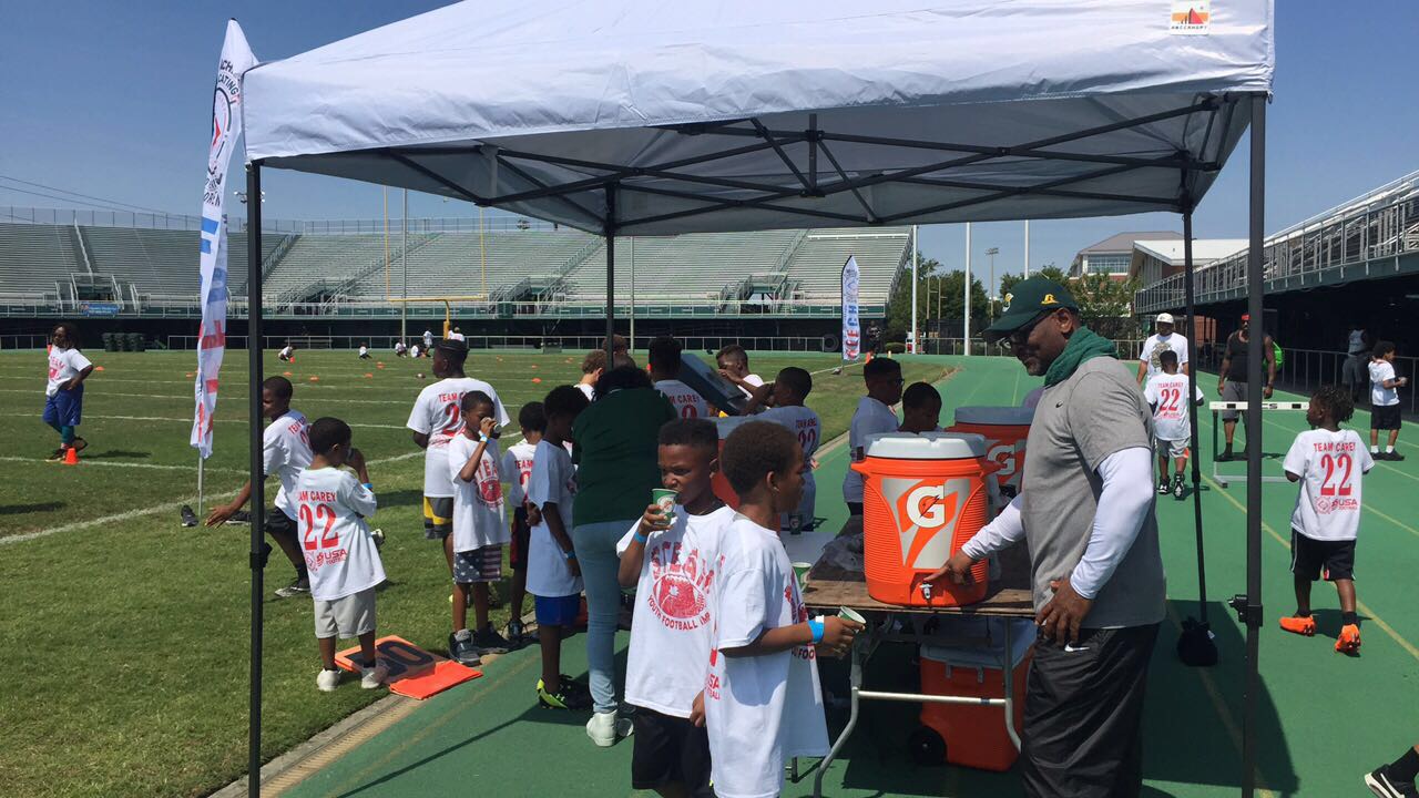 Alt text: "Kids in Team Carey jerseys gather under a tent for water and Gatorade at the STEAM Camp Football Day event.