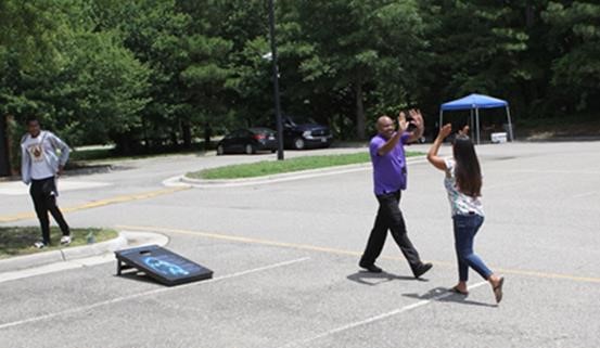 Two attendees high-fiving after a cornhole toss in the parking lot during the cookout.
